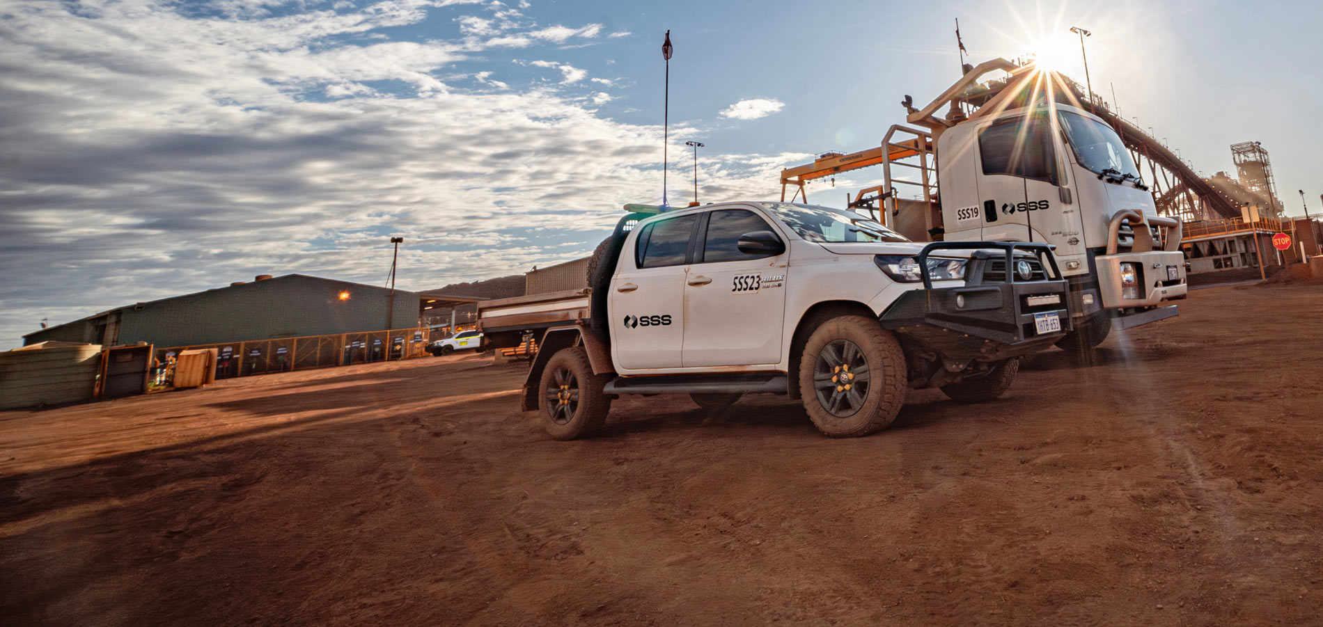 SSS Jeep and truck in an arid location, backlit by the sun